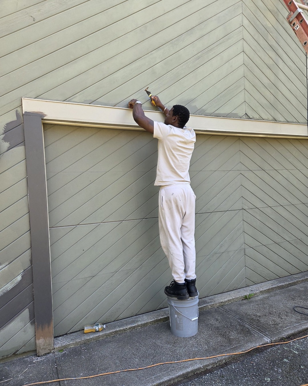Faded sage green chevron garage siding and door being scraped before exterior repainting