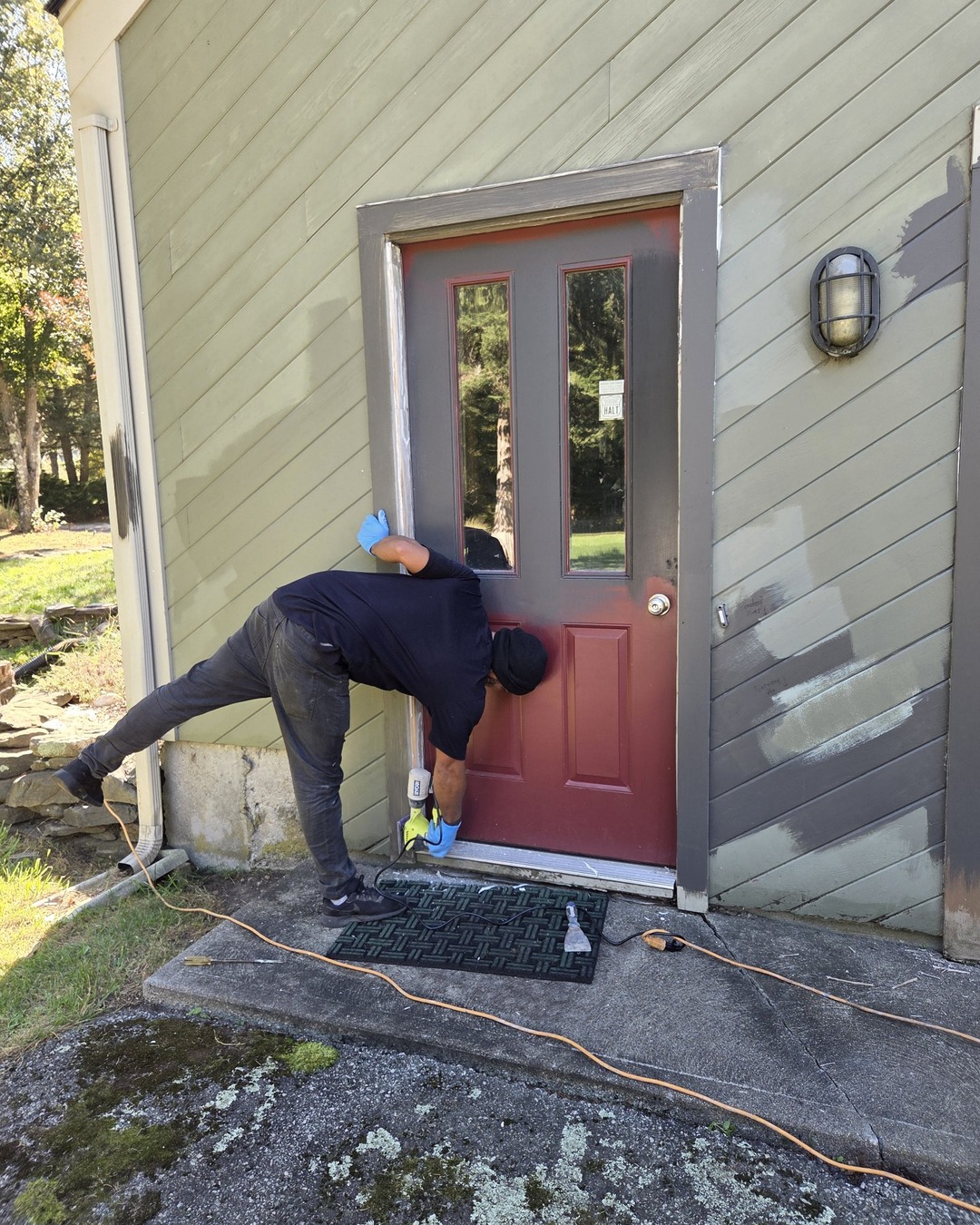 Side entry door in worn burgundy and faded green siding being sanded before repainting