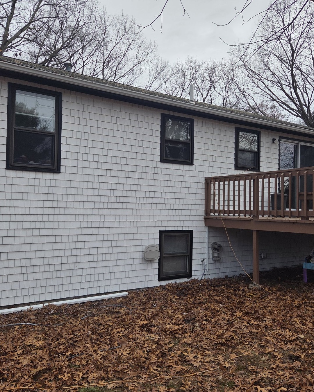 Rear of the shingle home after painting, showing finished off-white shingle siding and dark brown window frames and fascia beside an attached wooden deck